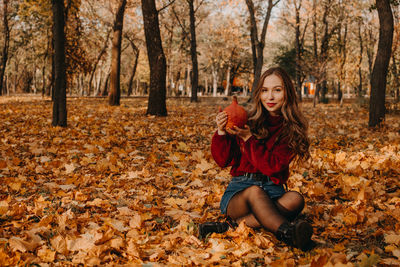 Young woman with dry leaves on ground during autumn
