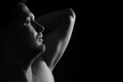 Close-up of shirtless man standing against black background