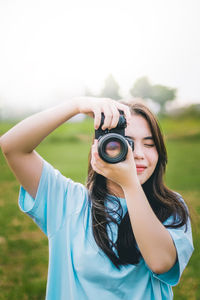 Young woman photographing through camera against sky