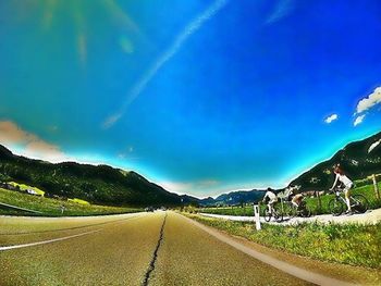 Empty road leading towards mountains against blue sky