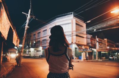 Rear view of woman wearing cap standing on road in city at night