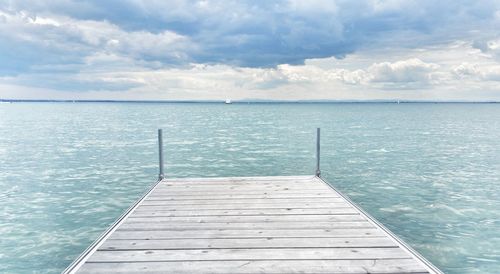 Pier by sea against cloudy sky