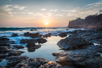 Rocks on beach against sky during sunset