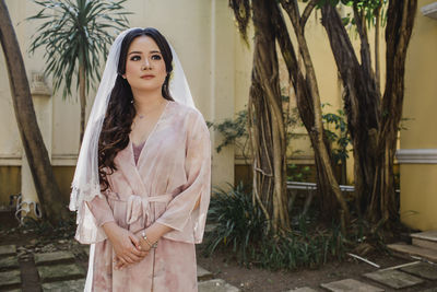 Young woman wearing bridal veil standing against tree