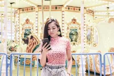 Woman using mobile phone against carousel
