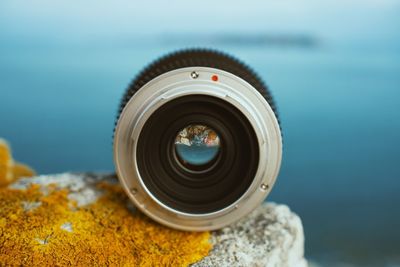 Close-up of camera lens against sea on rock