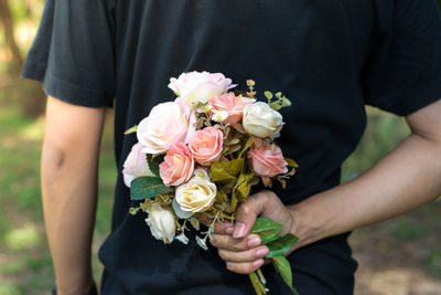 Midsection of man holding rose bouquet behind his back outdoors