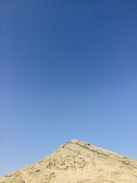 Low angle view of rocky mountain against clear blue sky