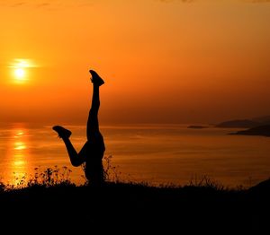 Silhouette person with arms raised against sky during sunset