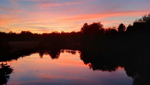 Silhouette trees by lake against sky during sunset