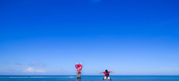 People standing in sea against clear blue sky