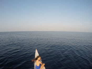 Woman sitting on boat at sea against clear sky