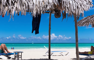 Low section of men lying on lounge chairs at beach during sunny day