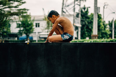 Side view of shirtless boy sitting outdoors