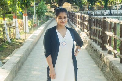 Portrait of smiling young woman standing on railing in city