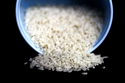 Close-up of scattered raw rice fallen from blue container against black background