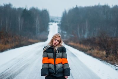 Portrait of young woman standing on snow covered road