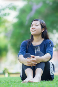 Smiling young woman looking away while sitting on grassy field at park