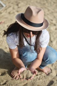 High angle view of woman holding sand while crouching at beach