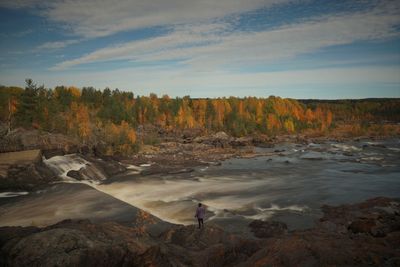 Man standing on rocks at shore against sky