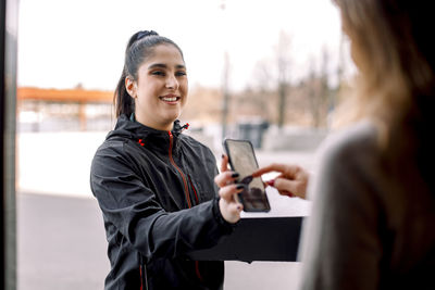 Woman signing on smart phone while receiving package from delivery woman