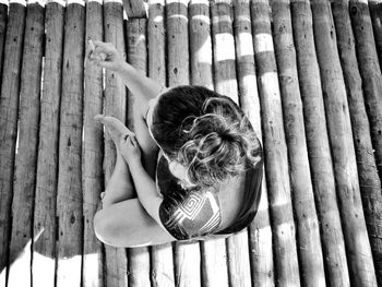 High angle view of woman sitting on boardwalk during sunny day