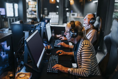 Elderly woman playing video game on computer by male friend at gaming lounge