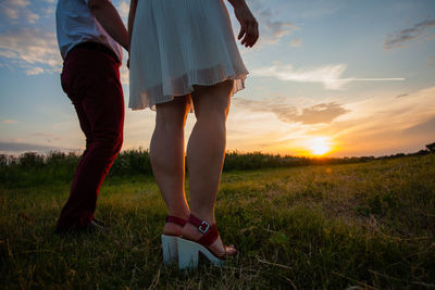 Low section of women standing on field against sky during sunset