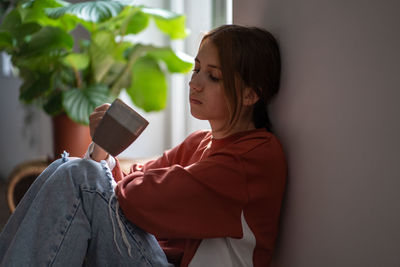 Frustrated teen girl sits on floor with cup sad devastated thinking about problems of broken heart