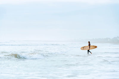 Side view of surfer man dressed in wetsuit walking looking away with surfboard towards the water to catch a wave on the beach during sunrise