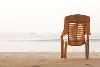 Empty chair on beach against clear sky