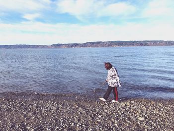 Rear view of boy standing on beach against sky