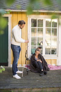 Woman using mobile phone while man holding fishing rod at summer house