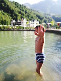 Shirtless boy gesturing stop while standing in lake