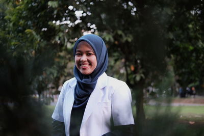 Portrait of smiling young woman wearing hijab standing against trees