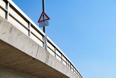 Low angle view of road sign against clear blue sky