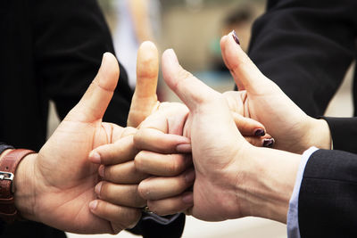 Cropped hands of business colleagues gesturing thumbs up in office