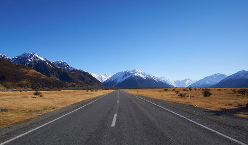 Road leading towards snow covered mountains against clear sky