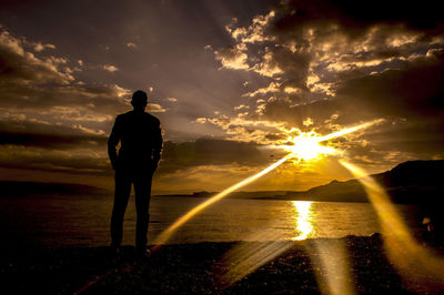 Rear view of silhouette man standing against sea during sunset