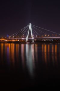 Illuminated bridge over river against sky at night