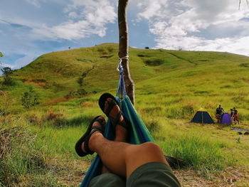 Low section of man relaxing on hammock against sky