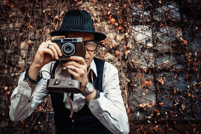 Retro-styled photographer taking picture with analog photo camera outdoors.