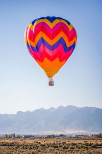 Colorful orange and blue hot air balloon flying above a mountain range desert landscape in nevada