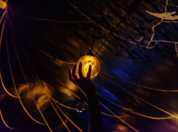 Cropped hand touching illuminated light bulb