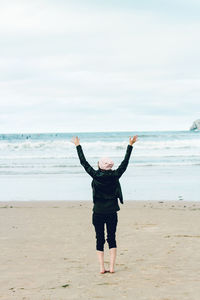 Rear view of woman standing on sand at beach against sky