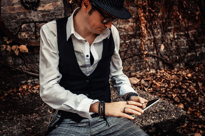 Retro-styled man with fedora hat surfing the net on digital tablet while relaxing outdoors.