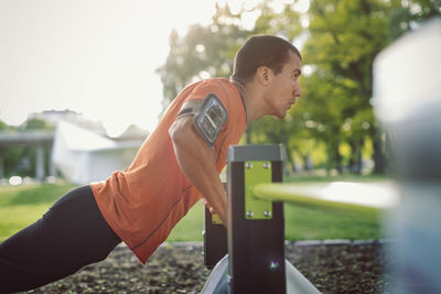 Side view of man doing push-ups on railing at park