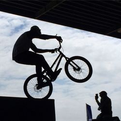 Silhouette man performing stunt on bicycle against sky