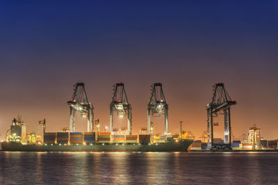 Cranes at commercial dock against sky at night