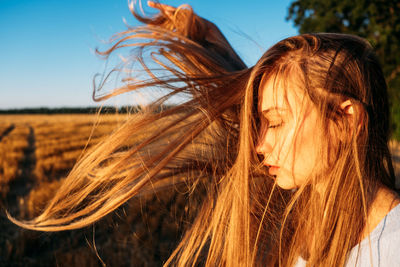 Peaceful woman with long hair in blue linen dress spending time in nature on summer day in sunset